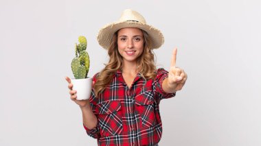 Çok zayıf bir kadın gülümsüyor ve dost canlısı görünüyor. Elinde kaktüs tutan bir numara var. çiftçi kavramı