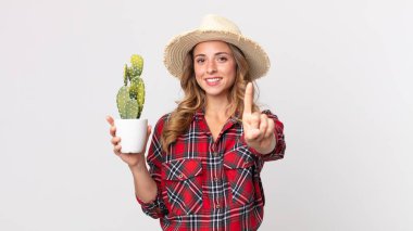 Oldukça zayıf bir kadın gururla gülümsüyor ve kaktüs tutarak bir numara yapıyor. çiftçi kavramı