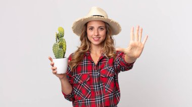 Çok zayıf bir kadın gülümsüyor ve dost canlısı görünüyor. Beş numara elinde kaktüs tutuyor. çiftçi kavramı