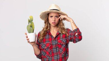 Kafası karışmış, kafası karışmış, elinde kaktüs tutan bir deli olduğunu gösteren ince bir kadın. çiftçi kavramı