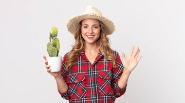 Oldukça zayıf bir kadın mutlu bir şekilde gülümsüyor, el sallıyor, seni selamlıyor ve bir kaktüs tutuyor. çiftçi kavramı