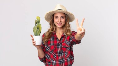 Çok zayıf bir kadın gülümsüyor ve dost canlısı görünüyor. İki numara elinde kaktüs tutuyor. çiftçi kavramı