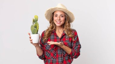 Oldukça zayıf bir kadın neşeli bir şekilde gülümsüyor, mutlu hissediyor ve elinde kaktüs tutan bir konsept gösteriyor. çiftçi kavramı