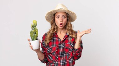 Oldukça zayıf bir kadın şaşırmış ve şok olmuş görünüyor. Elinde kaktüs tutan bir nesneyi çenesi düşmüş. çiftçi kavramı