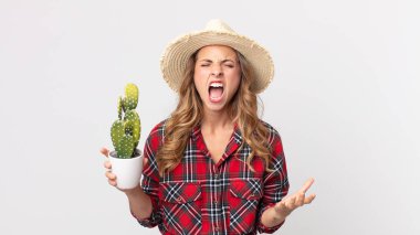 Oldukça zayıf bir kadın saldırganca bağırıyor, elinde kaktüs tutarken çok kızgın görünüyor. çiftçi kavramı