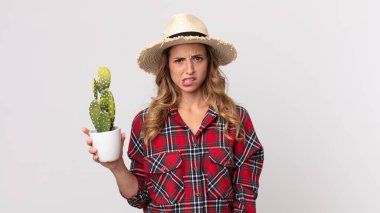 Oldukça zayıf bir kadın elinde kaktüs tutarken şaşkın ve kafası karışmış hissediyor. çiftçi kavramı