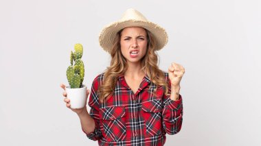 Oldukça zayıf bir kadın elinde kaktüs tutan kızgın bir ifadeyle agresif bir şekilde bağırıyor. çiftçi kavramı