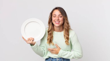 Oldukça zayıf bir kadın komik bir şakaya yüksek sesle gülüyor ve elinde boş bir tabakla boş bir tabak tutuyor.