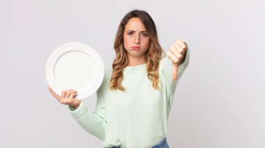 Çapraz hisseden oldukça zayıf bir kadın, baş parmaklarını gösteriyor ve boş bir tabak tutuyor ve boş bir tabak tutuyor.