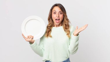 Oldukça zayıf bir kadın kendini mutlu ve şaşkın hissediyor inanılmaz bir şey ve boş bir tabak tutuyor ve boş bir tabak tutuyor.