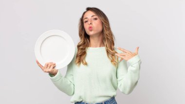 Oldukça zayıf bir kadın stresli, endişeli, yorgun ve hayal kırıklığına uğramış ve elinde boş bir tabakla boş bir tabak tutuyor.