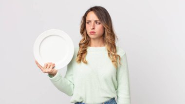 Oldukça zayıf bir kadın üzgün, üzgün ya da kızgın ve yana bakıyor boş bir tabak tutuyor ve boş bir tabak tutuyor.