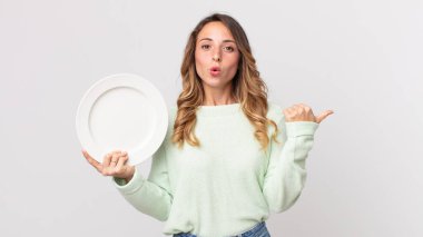 İnançsızlıktan şaşkın bakan, boş bir tabak tutan ve elinde boş bir tabak tutan zayıf bir kadın.