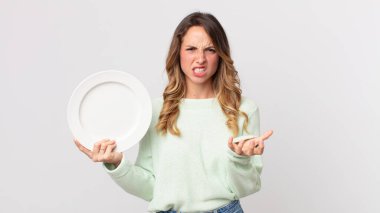 Oldukça zayıf bir kadın kızgın, sinirli ve hayal kırıklığına uğramış görünüyor ve elinde boş bir tabakla boş bir tabak tutuyor.