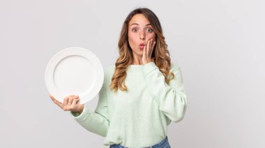 Oldukça zayıf bir kadın şok olmuş ve korkmuş hissediyor ve elinde boş bir tabakla boş bir tabak tutuyor.