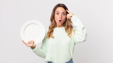 Oldukça zayıf bir kadın şaşırmış görünüyor, yeni bir düşünce, fikir ya da konsept fark ediyor ve boş bir tabak tutuyor ve boş bir tabak tutuyor.