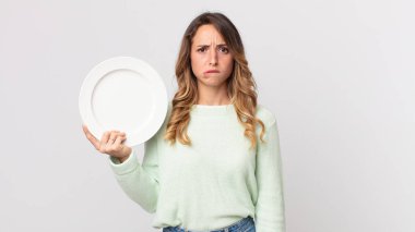 Kafası karışmış, kafası karışmış, elinde boş bir tabak tutan ve elinde boş bir tabak tutan oldukça zayıf bir kadın.