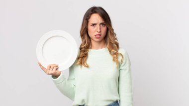 Kafası karışmış, kafası karışmış, elinde boş bir tabak tutan ve elinde boş bir tabak tutan zayıf bir kadın.