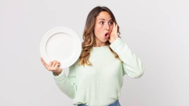 Oldukça zayıf bir kadın kendini mutlu, heyecanlı ve şaşırmış hissediyor ve elinde boş bir tabakla boş bir tabak tutuyor.