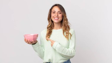 Oldukça zayıf bir kadın neşeli bir şekilde gülümsüyor, mutlu hissediyor ve bir tarafı işaret ediyor ve elinde boş bir tencere tutuyor.