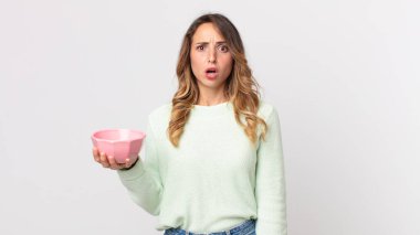 Oldukça zayıf bir kadın şok olmuş ya da şaşırmış görünüyor ve elinde boş bir tencere tutuyor.