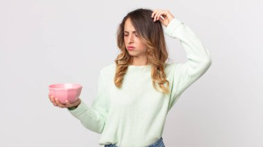 Kafası karışmış, kafası karışmış, kafasını kaşıyan ve elinde boş bir tencere tutan oldukça zayıf bir kadın.