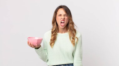 Oldukça zayıf bir kadın agresif bir şekilde bağırıyor, kızgın görünüyor ve elinde boş bir tencere tutuyor.