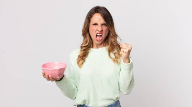 Oldukça zayıf bir kadın kızgın bir ifadeyle agresif bir şekilde bağırıyor ve elinde boş bir saksı tutuyor.