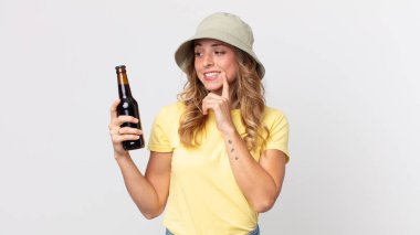 Oldukça zayıf bir kadın mutlu bir şekilde gülümsüyor ve hayal kuruyor ya da şüphe ediyor ve elinde bira tutuyor. yaz konsepti