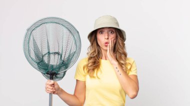 Oldukça zayıf bir kadın şok olmuş ve korkmuş hissediyor. Şapka takıyor ve elinde balık ağı tutuyor.