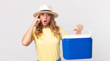 Oldukça zayıf bir kadın şaşırmış görünüyor, yeni bir düşünce, fikir ya da konsept fark ediyor ve elinde bir yaz pikniği buzdolabı tutuyor.