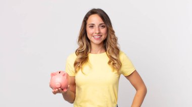 Oldukça zayıf bir kadın mutlu bir şekilde gülümsüyor, eli kalçasında, kendinden emin ve kumbarasını tutuyor.