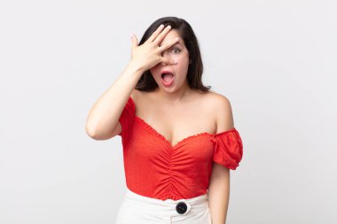 Güzel bir kadın şok olmuş, korkmuş ya da korkmuş görünüyor. Yüzü elle örtülmüş ve parmaklarının arasından gizlice bakıyor.