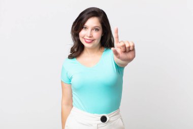 Güzel bir kadın gülümsüyor ve arkadaş canlısı görünüyor. Bir numarayı gösteriyor ya da ilk eli önde, geri sayıyor.