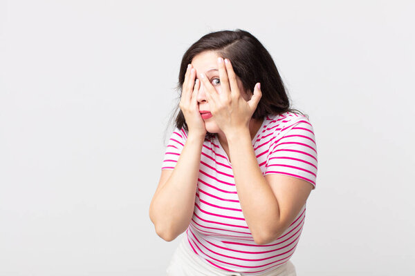 красивая женщина чувствует себя испуганной или смущенной, подглядывает или шпионит с глазами, наполовину покрытыми руками