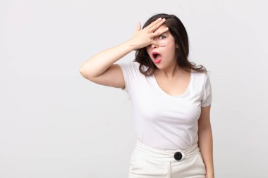 Güzel bir kadın şok olmuş, korkmuş ya da korkmuş görünüyor. Yüzü elle örtülmüş ve parmaklarının arasından gizlice bakıyor.