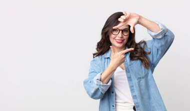 Güzel bir kadın mutlu, arkadaş canlısı ve pozitif hissediyor, gülümsüyor ve elleriyle bir portre veya fotoğraf çerçevesi yapıyor.