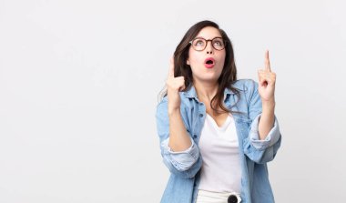 Güzel bir kadın şaşırmış, şaşırmış ve ağzı açık görünüyor, iki eliyle uzayı işaret ediyor.