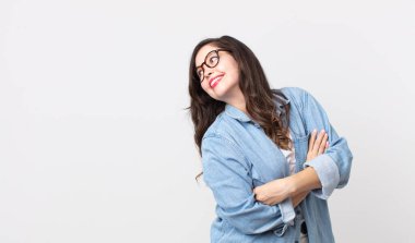 Güzel bir kadın neşeyle gülümsüyor, mutlu, tatmin olmuş ve rahatlamış hissediyor, kollarını kavuşturup yan tarafa bakıyor.