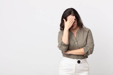 Güzel bir kadın stresli, utanmış ya da üzgün görünüyor, baş ağrısı var, yüzünü elleriyle kapatıyor.