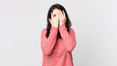 Güzel bir kadın elleriyle yüzünü kapatıyor, parmaklarının arasından şaşkın bir ifadeyle yan tarafa bakıyor.