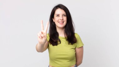 Güzel bir kadın gülümsüyor ve arkadaş canlısı görünüyor. İki ya da iki numarayı gösteriyor. Elleri önde, geri sayıyor.