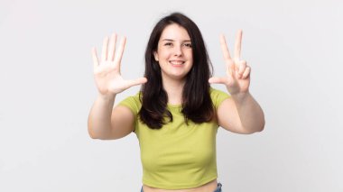 Güzel bir kadın gülümsüyor ve arkadaş canlısı görünüyor, 8 ya da 8 numarayı gösteriyor, elleri önde, geriye doğru sayıyor.