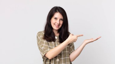 Güzel bir kadın neşeyle gülümsüyor ve yan taraftaki fotokopi alanını işaret ediyor, bir nesneyi gösteriyor ya da reklamını yapıyor.