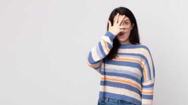 Güzel bir kadın şok olmuş, korkmuş ya da korkmuş görünüyor. Yüzü elle örtülmüş ve parmaklarının arasından gizlice bakıyor.