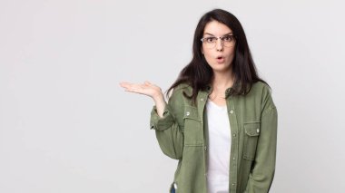 Güzel bir kadın şaşırmış ve şoka uğramış görünüyor, çenesi düşmüş, elinde açık bir elle bir nesne tutuyor.