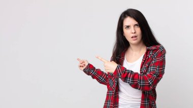 Güzel bir kadın şaşkın ve şaşırmış hissediyor. Kenardaki fotokopi alanını işaret ediyor. Şaşırmış, ağzı açık bir şekilde bakıyor.