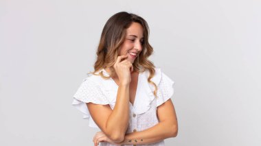 Oldukça zayıf bir kadın mutlu, kendinden emin bir ifadeyle gülümsüyor, elleri çenesinde, merak ediyor ve yan tarafa bakıyor.