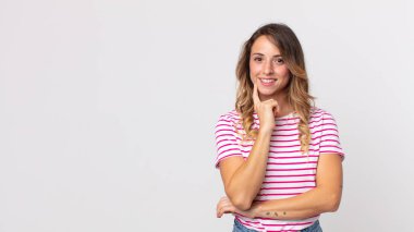 Oldukça zayıf bir kadın mutlu görünüyor ve gülümsüyor, eli çenesinde, merak ediyor ya da soru soruyor, seçenekleri karşılaştırıyor.