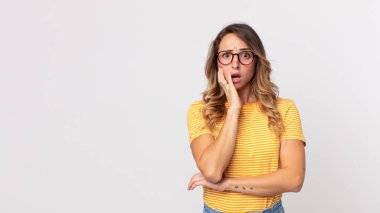 Oldukça ince bir kadın şok ve inanmazlık içinde, elleri yanağında ve kolları çaprazlanmış, sersemlemiş ve şaşırmış hissediyor.